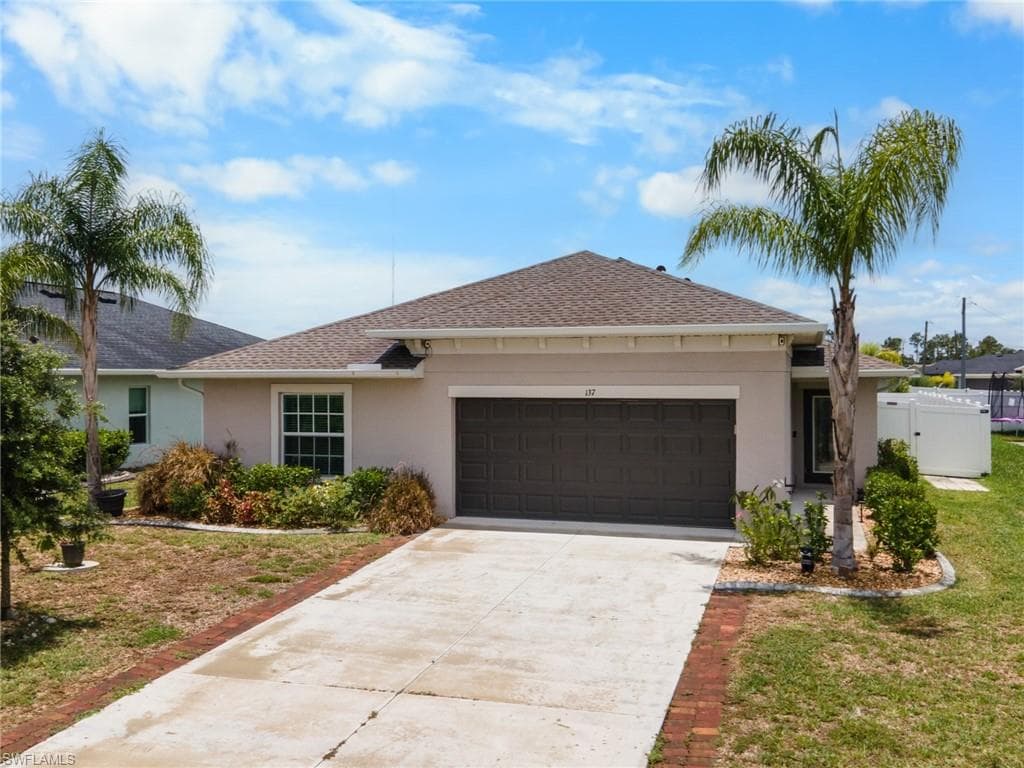 Single-story residence featuring a two-car garage, concrete driveway with brick paver accents, and a shingle roof