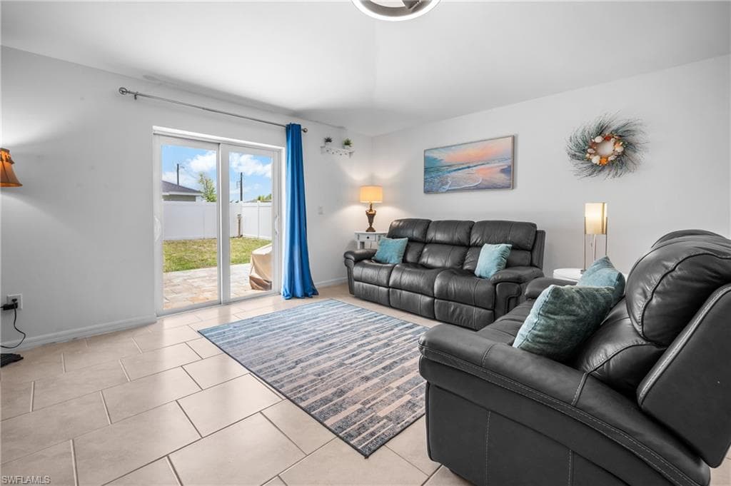 Living area with tile flooring, white walls, and sliding glass doors opening to a fenced backyard