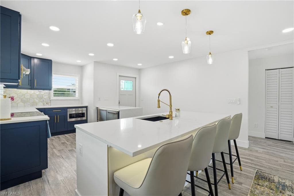 Kitchen featuring blue cabinetry, a kitchen island with sink, pendant lighting, recessed lighting, and decorative backsplash - Virtually Edited Image