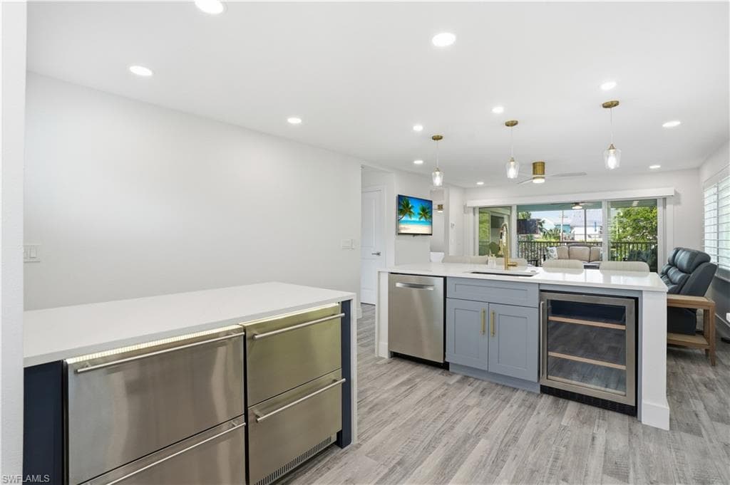 Kitchen with beverage cooler, open floor plan, hanging light fixtures, light stone counters, and recessed lighting - Virtually Edited Image