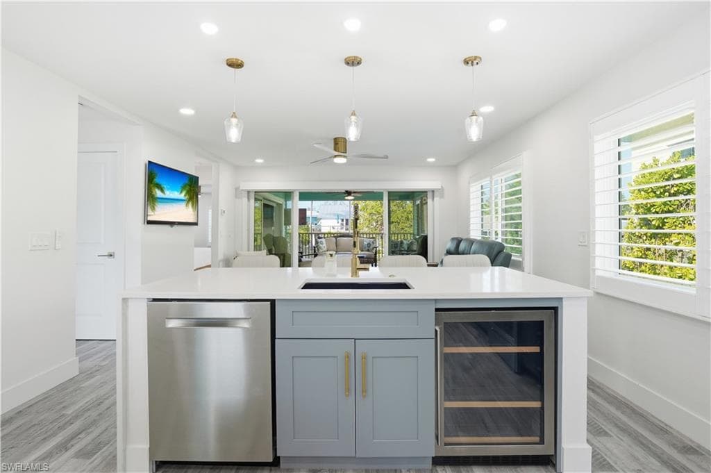 Kitchen featuring beverage cooler, dishwasher, an island with sink, open floor plan, and a ceiling fan - Virtually Edited Image
