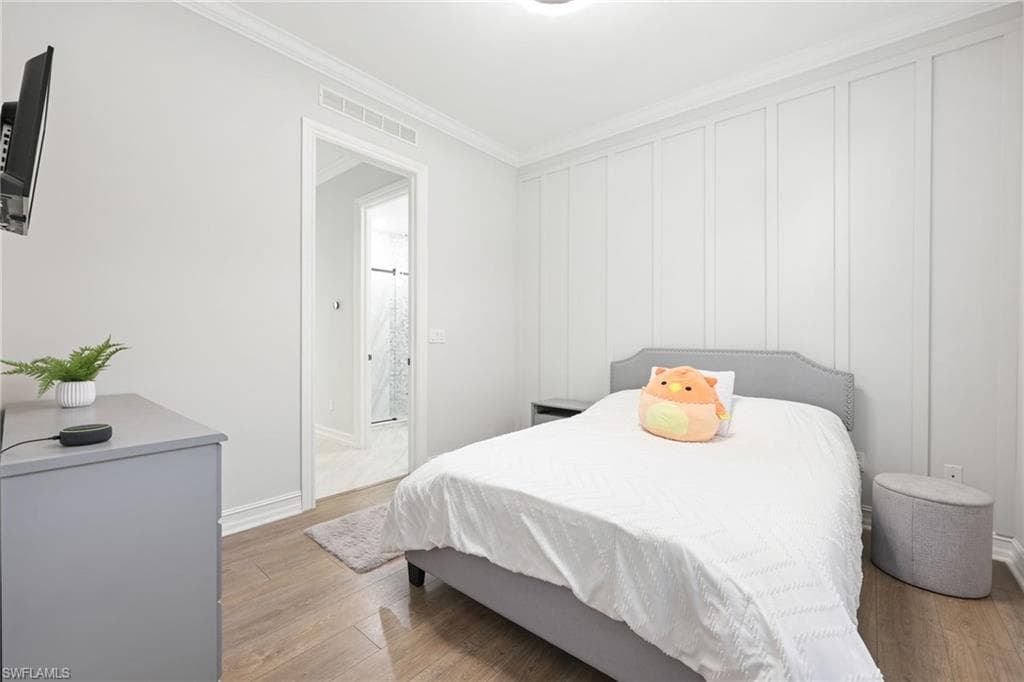 Bedroom featuring wood-finish flooring, crown molding, and a board and batten accent wall