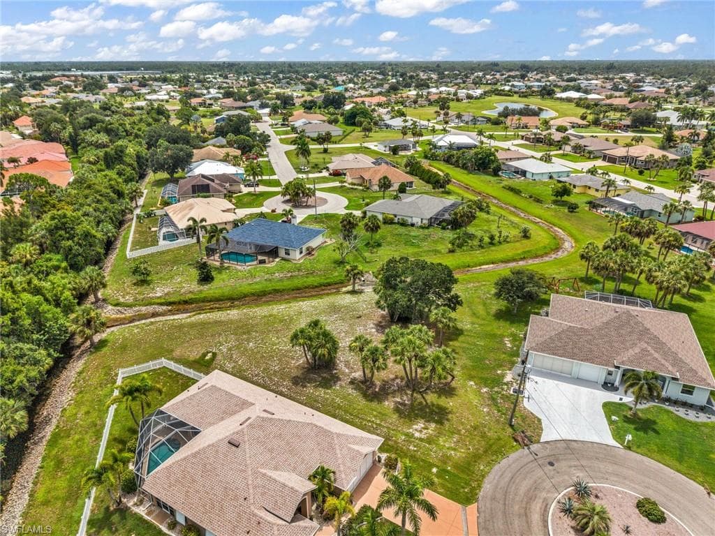 Aerial perspective showcasing multiple properties with screened pools, lush green lawns, mature palm trees, and cul-de-sac street designs