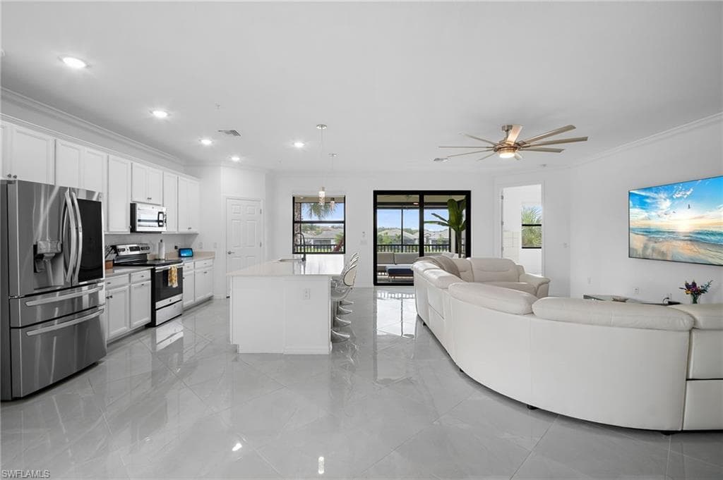 Open-concept living area featuring a kitchen with stainless steel appliances, white cabinetry, and a center island with seating