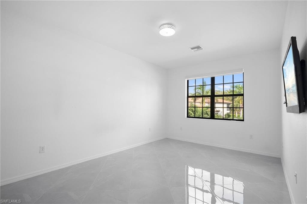 Spacious room featuring light gray tile flooring, crisp white walls, and a large window with black grilles