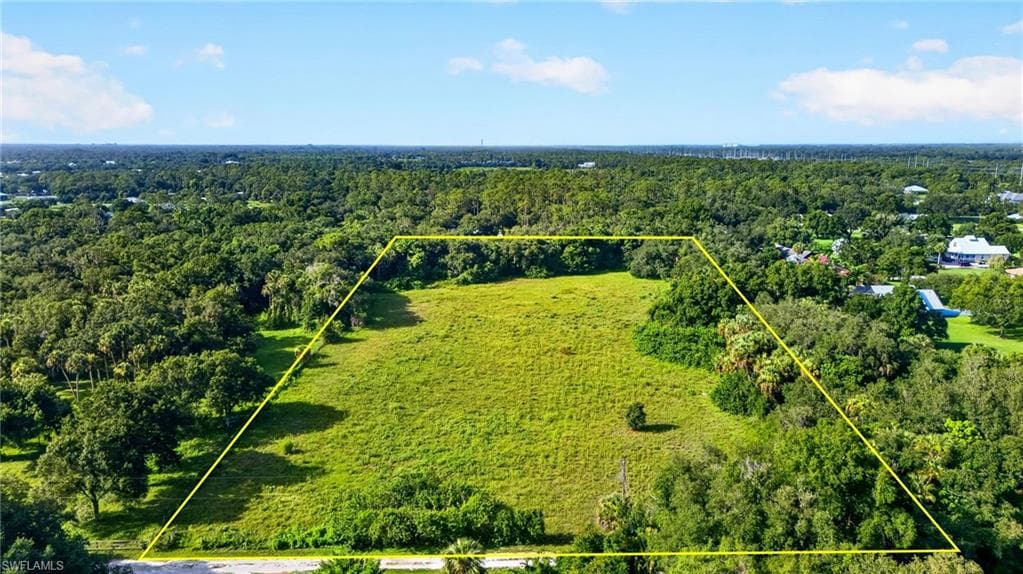 Expansive land parcel featuring a central grassy area and surrounding mature trees