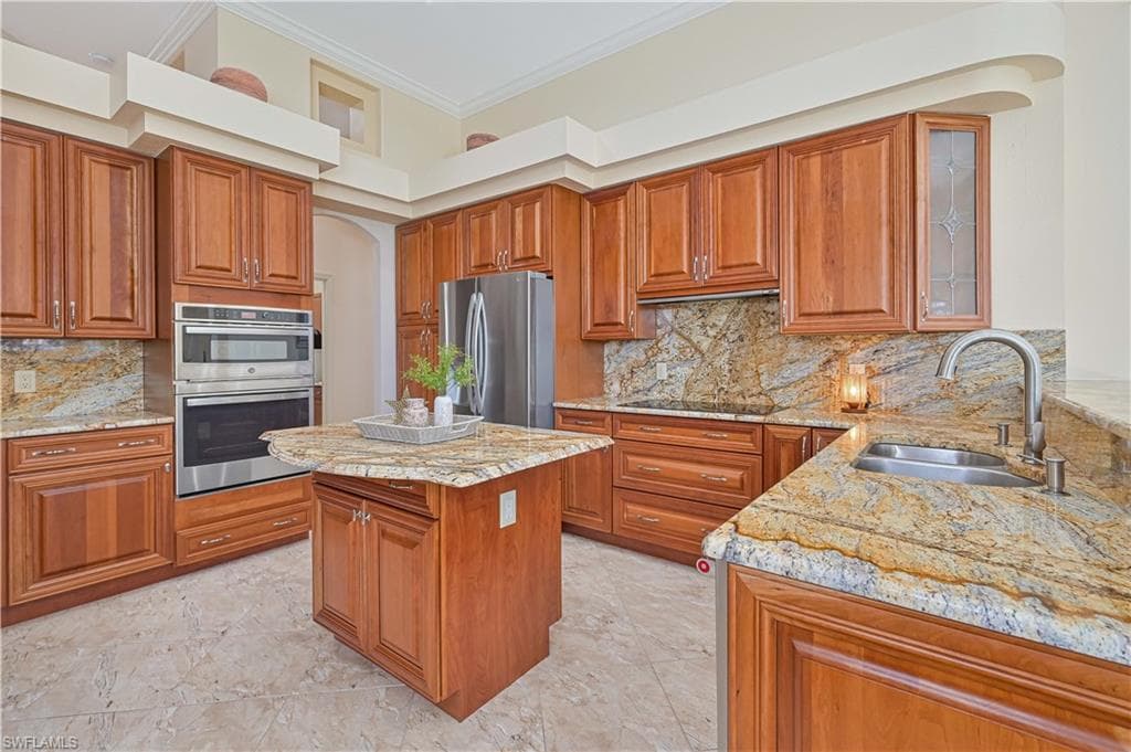 Gourmet kitchen with wood cabinetry, stainless steel appliances, a center island, stone countertops, and tile flooring