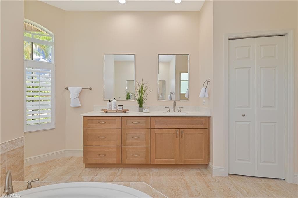 Double vanity featuring light wood-finish cabinetry, a light-toned countertop, and dual mirrors