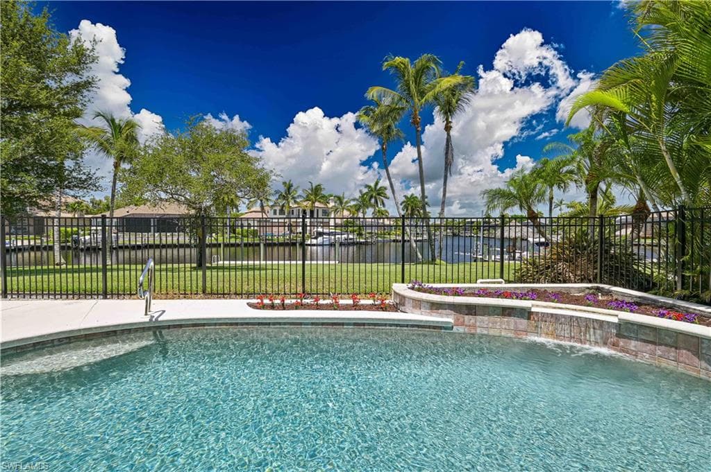 Resort-style pool area featuring a curved deck, integrated waterfall, and tiered planter with various foliage