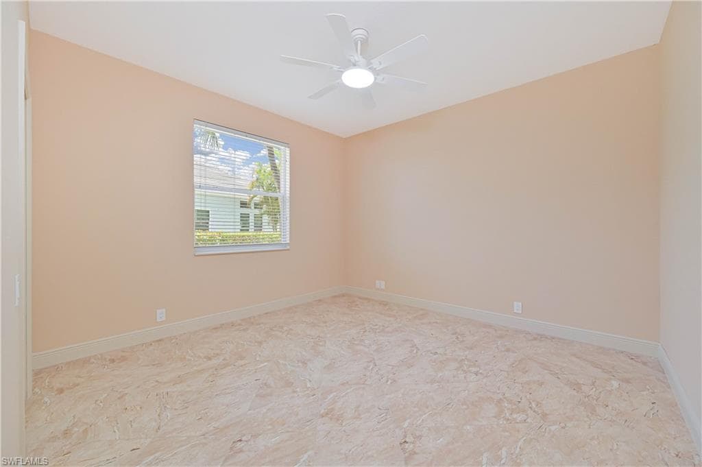 Spacious room featuring neutral wall tones, large window with blinds, ceiling fan, and light-toned tile flooring