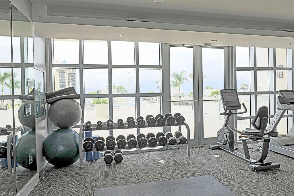 Fitness center featuring floor-to-ceiling windows, patterned carpet flooring, a mirrored wall, a dumbbell rack, and exercise equipment