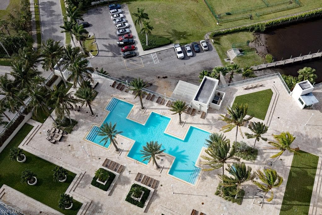 Expansive outdoor amenity space featuring a multi-level swimming pool with integrated steps, surrounding lounge areas, mature palm trees, and manicured green spaces