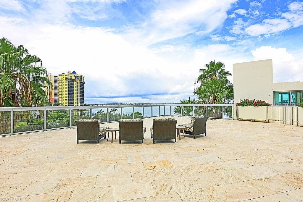 Expansive tiled patio featuring a glass railing system and water backdrop