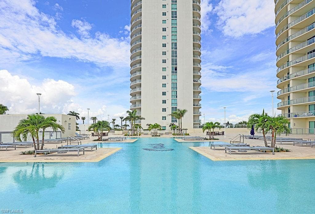 Expansive resort-style pool featuring multiple swimming areas, integrated lounging platforms, and surrounding palm trees