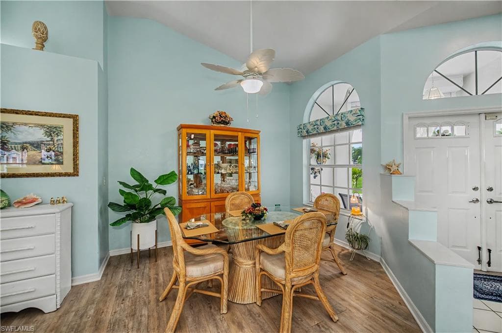 Bright dining area featuring vaulted ceilings, wood-finish flooring, a contemporary ceiling fan, and large windows with arched transoms