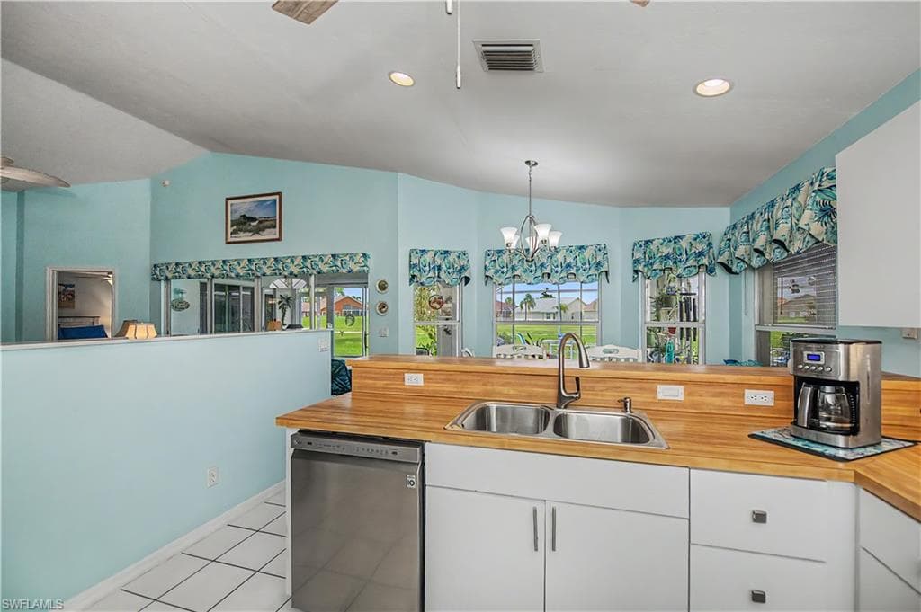 Kitchen featuring wood-finish countertops, a double stainless steel sink with a high-arc faucet, and white cabinetry
