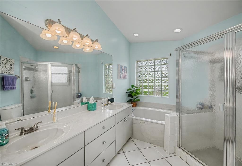 Spacious bathroom featuring a dual vanity with integrated sinks, a large mirror, a glass-enclosed shower, a built-in tub, and a glass block window