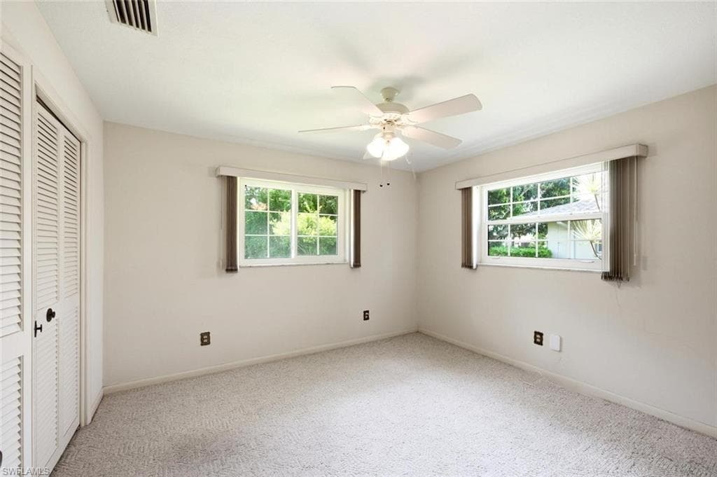 Spacious room featuring neutral carpeting, two large windows with horizontal blinds, and a ceiling fan with integrated lighting