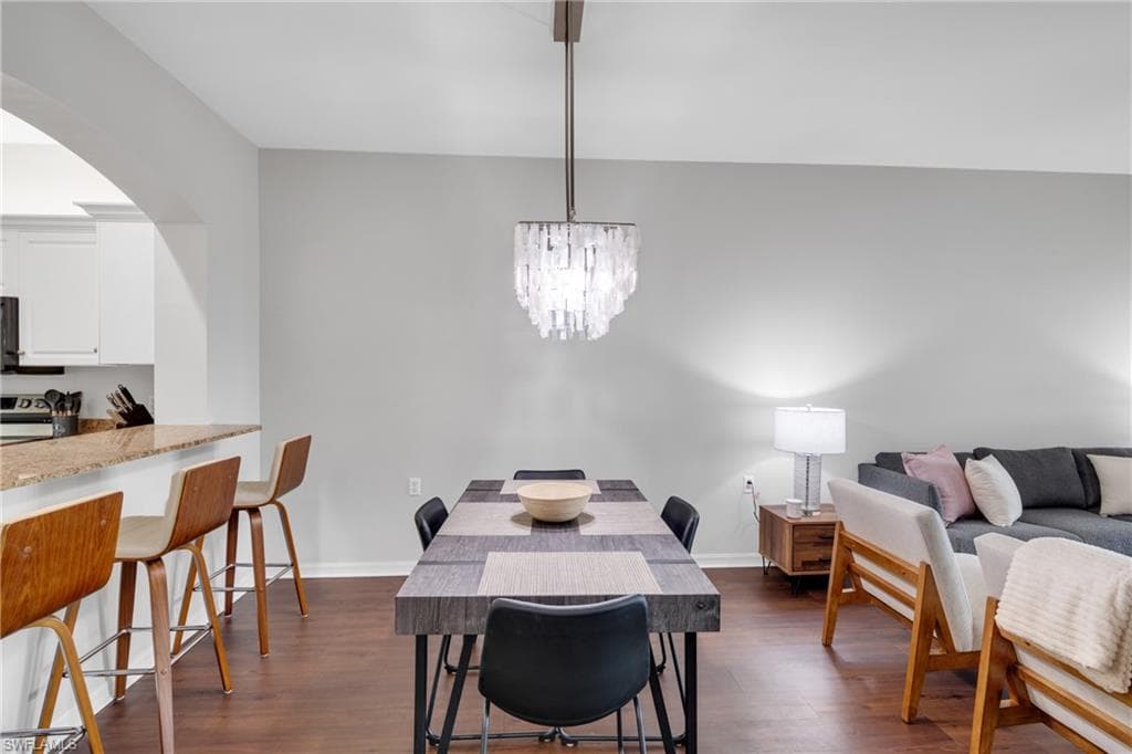 Open-concept living area featuring rich wood-finish flooring, a modern chandelier, and a kitchen pass-through with a granite-look countertop