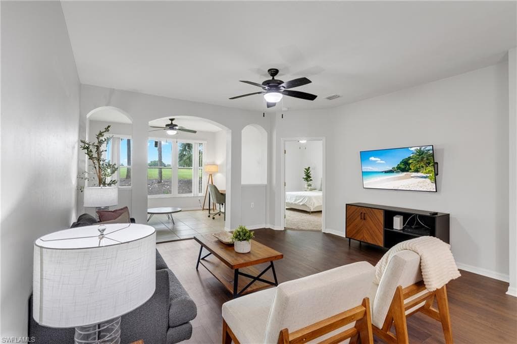 Spacious living area featuring wood-finish flooring, white walls, and a ceiling fan with integrated lighting