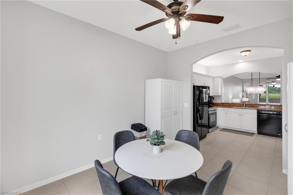 Arched doorway leading to the kitchen with white cabinetry, dark appliances, and a light-colored countertop