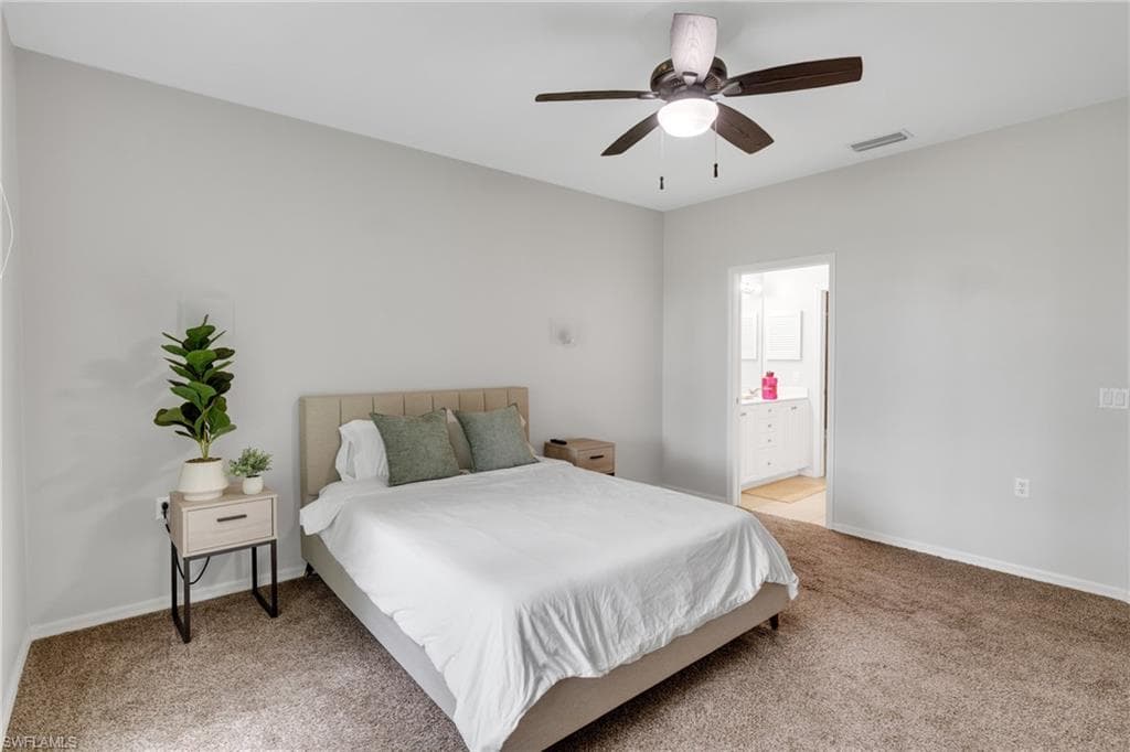 Carpeted room featuring a ceiling fan with integrated lighting, neutral wall tones, and an open doorway revealing a bathroom with a white vanity and mirror