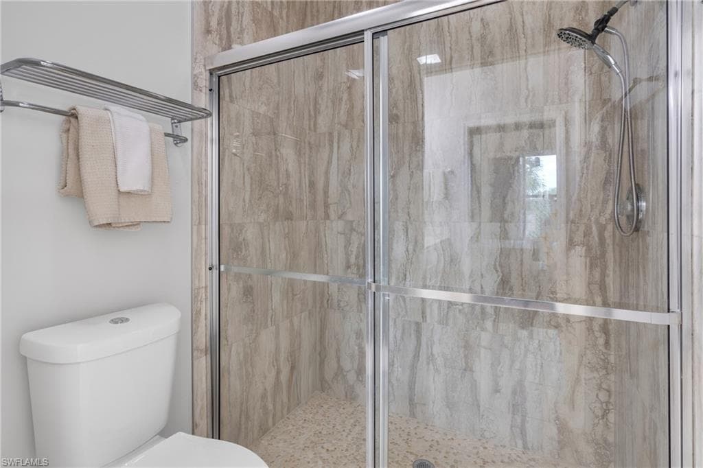 Shower enclosure with glass sliding doors, textured tile surround, and a pebble-style floor