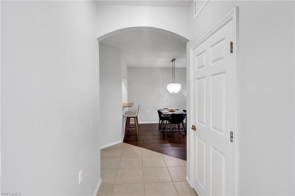 Entryway featuring light-toned tile flooring, an arched doorway, and a white paneled door with brass hardware