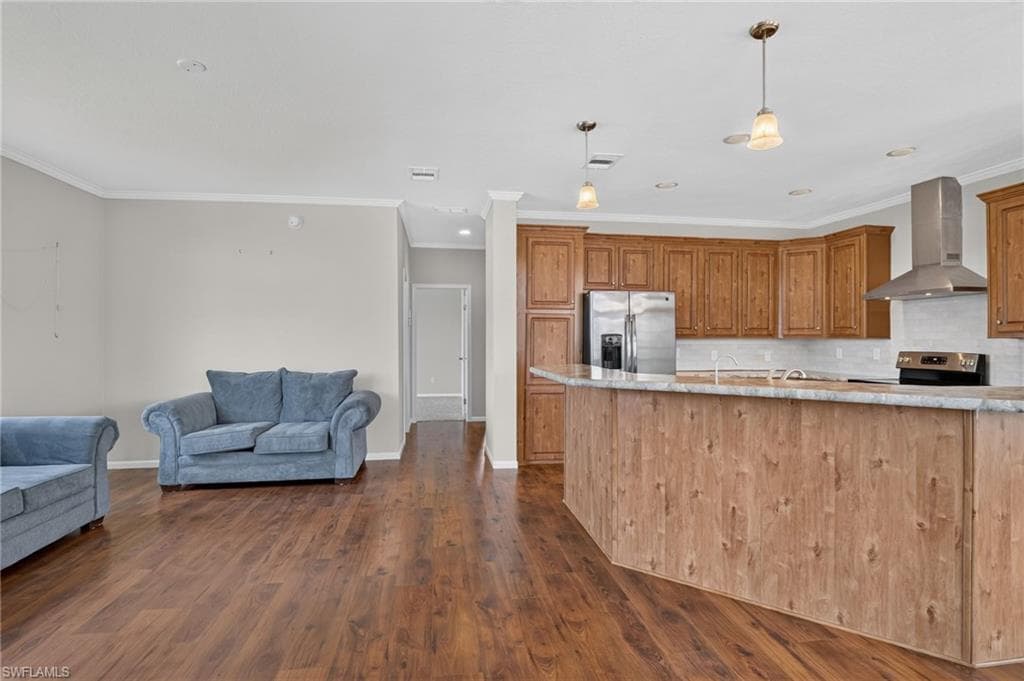 Open-concept living area featuring wood-finish flooring, a kitchen island with a wood-finish base, stainless steel appliances, a range hood, and pendant lighting