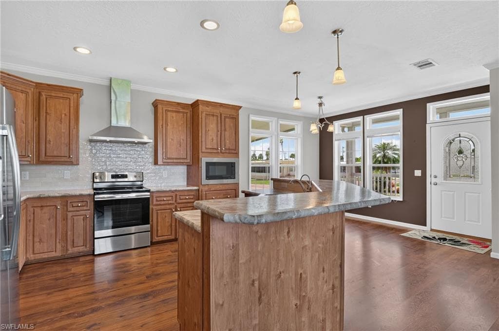 Open-concept kitchen featuring wood-finish cabinetry, stainless steel appliances, a center island with a sink, recessed lighting, and multiple windows