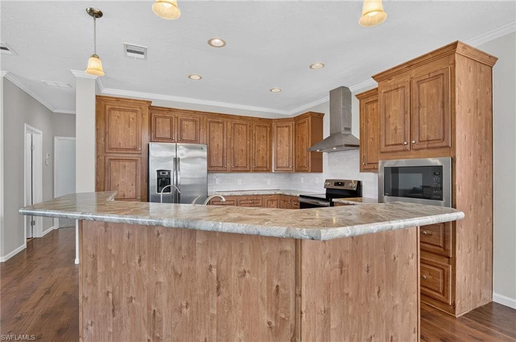 Kitchen featuring a large eat-at island, perimeter wood cabinetry, stainless steel appliances, and wood-finish flooring