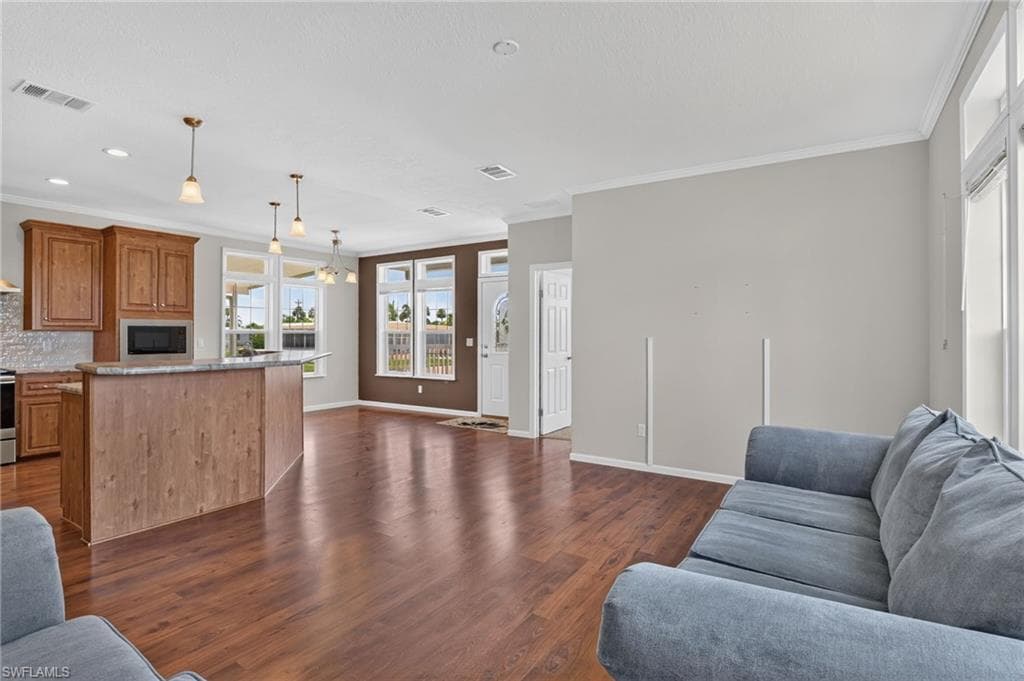Open-concept living space featuring wood-finish flooring, a kitchen island with pendant lighting, recessed lighting, crown molding, and multiple windows