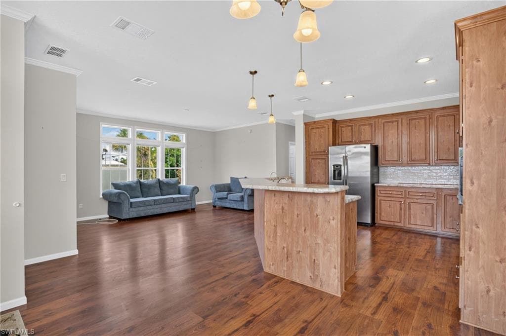 Open-concept living space featuring wood-finish flooring, ample natural light from multiple windows, a kitchen island with a stone-finish countertop, stainless steel appliances, and extensive wood cabinetry