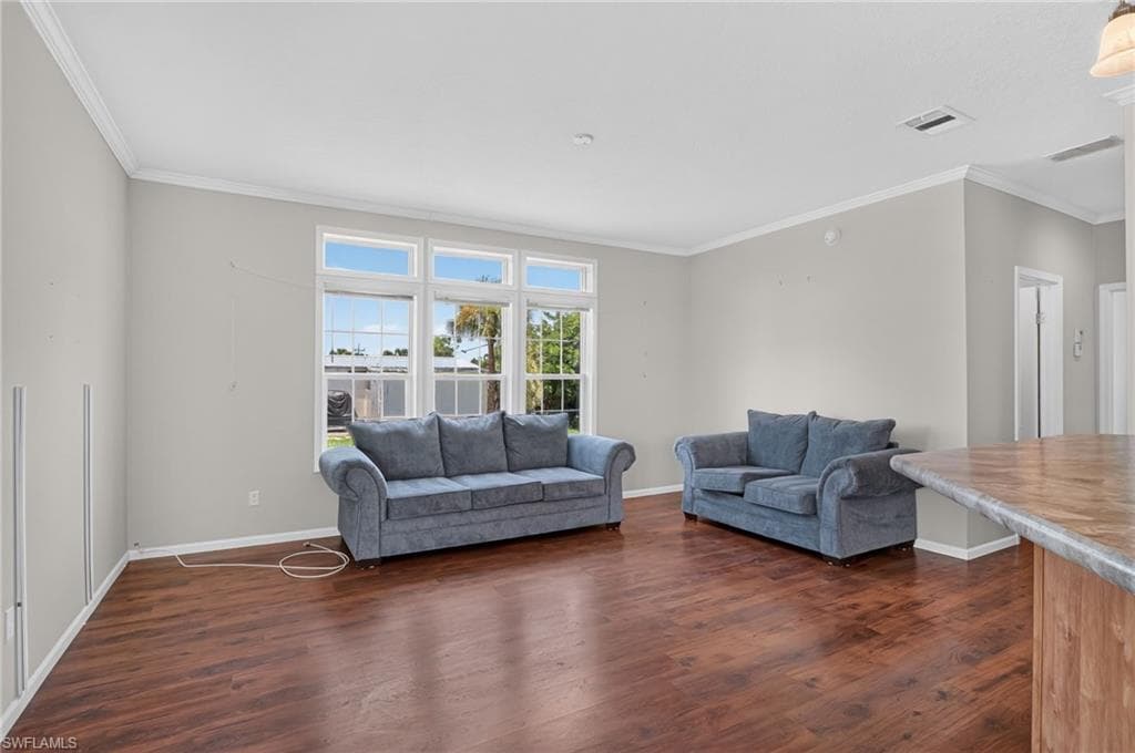 Spacious common area featuring rich wood-finish flooring, light gray walls, and white crown molding
