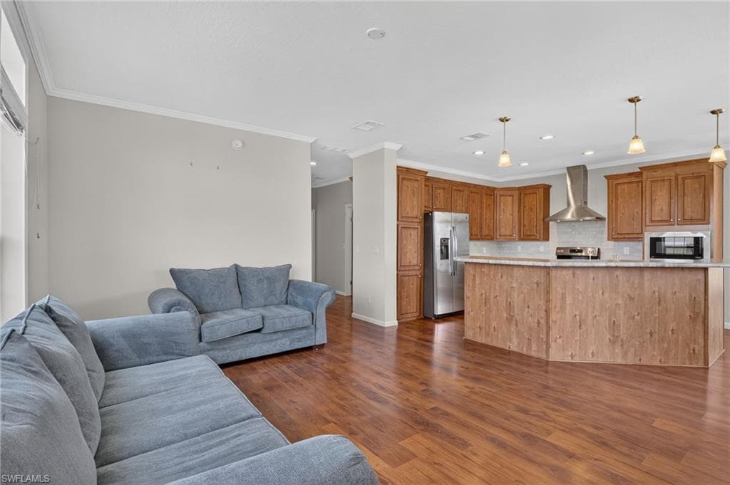 Open-concept living space featuring wood-finish flooring, a kitchen with wood cabinetry and stainless steel appliances, a kitchen island with pendant lighting, and light-toned walls