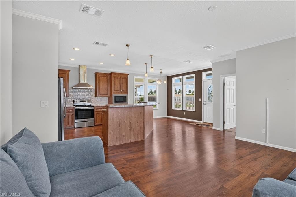 Open-concept living area featuring rich wood-finish flooring, recessed lighting, crown molding, and a kitchen island with pendant lighting