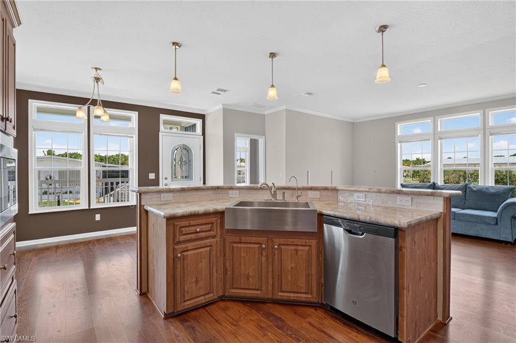 Kitchen island with a stainless steel farmhouse sink, integrated dishwasher, and pendant lighting