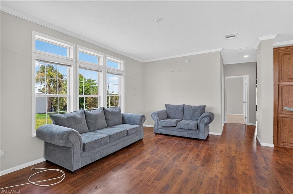 Spacious living area featuring large windows with white muntins, wood-finish flooring, light gray wall paint, white baseboards, and white crown molding