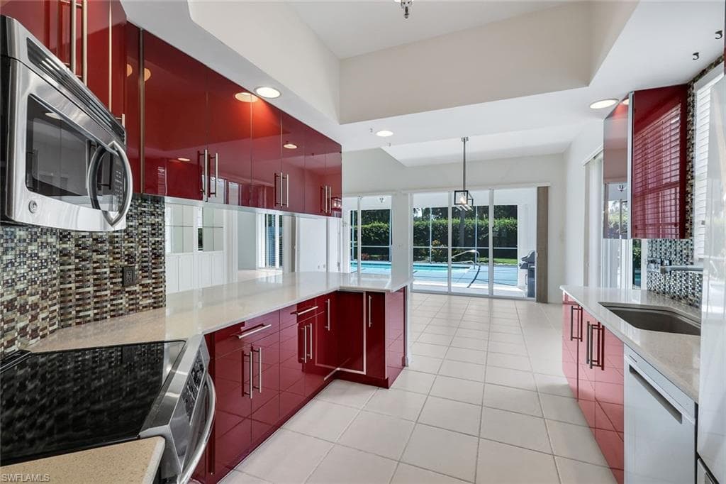 Kitchen featuring custom cabinetry, stainless steel appliances, tile backsplash, and light-toned quartz countertops. Overlooking the private pool.