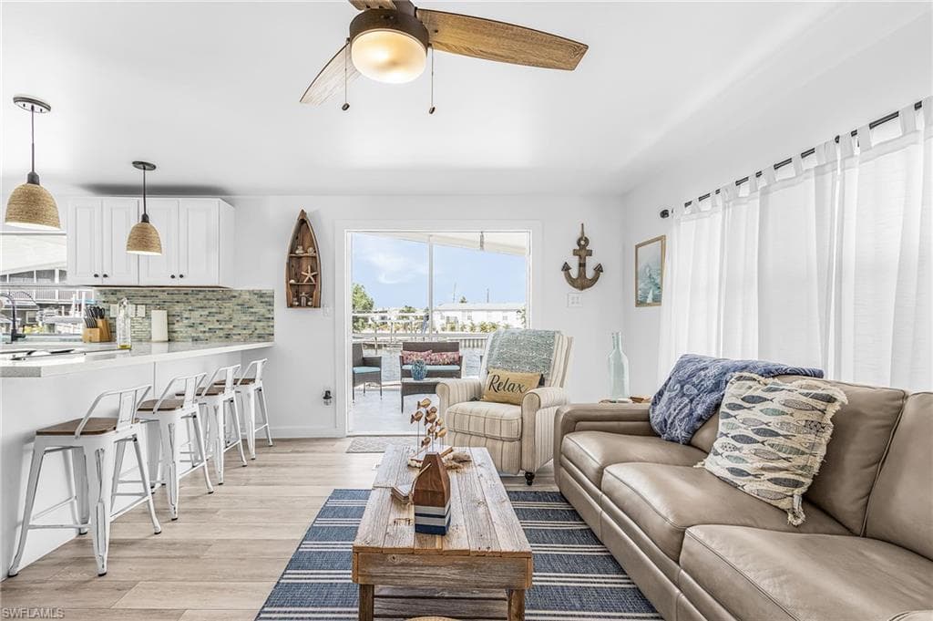 Open-concept living space featuring wood-finish flooring, a white kitchen island with pendant lighting, a tiled backsplash, and a sliding glass door leading to an outdoor patio