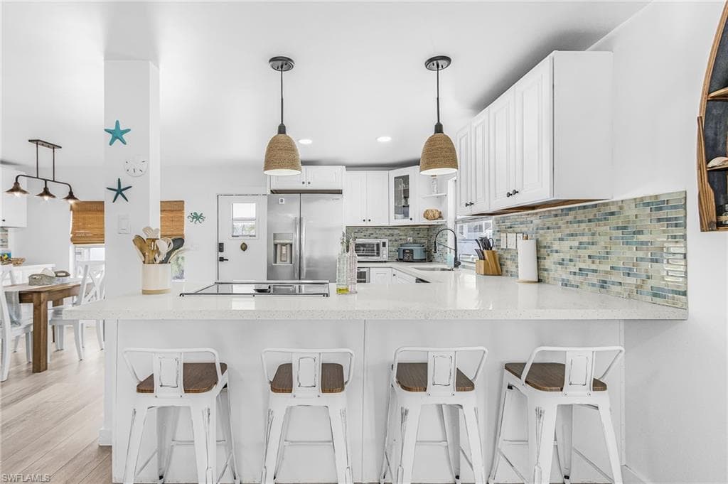 Kitchen featuring a white countertop island with integrated cooktop, pendant lighting, stainless steel refrigerator, white cabinetry, and a mosaic tile backsplash