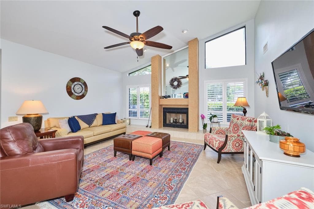 Living room featuring high vaulted ceiling, a large wood burning fireplace, light tile patterned floors, and lighted ceiling fan