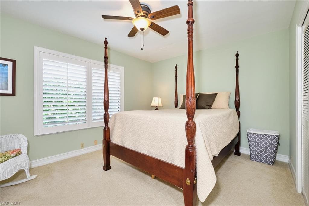 Guest bedroom with plantation shutters, carpet floors, and a lighted ceiling fan