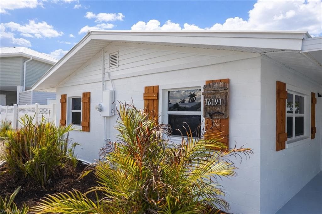Exterior featuring white siding and block construction, wood-finish shutters, white-framed windows, a decorative address plaque, and manicured landscaping