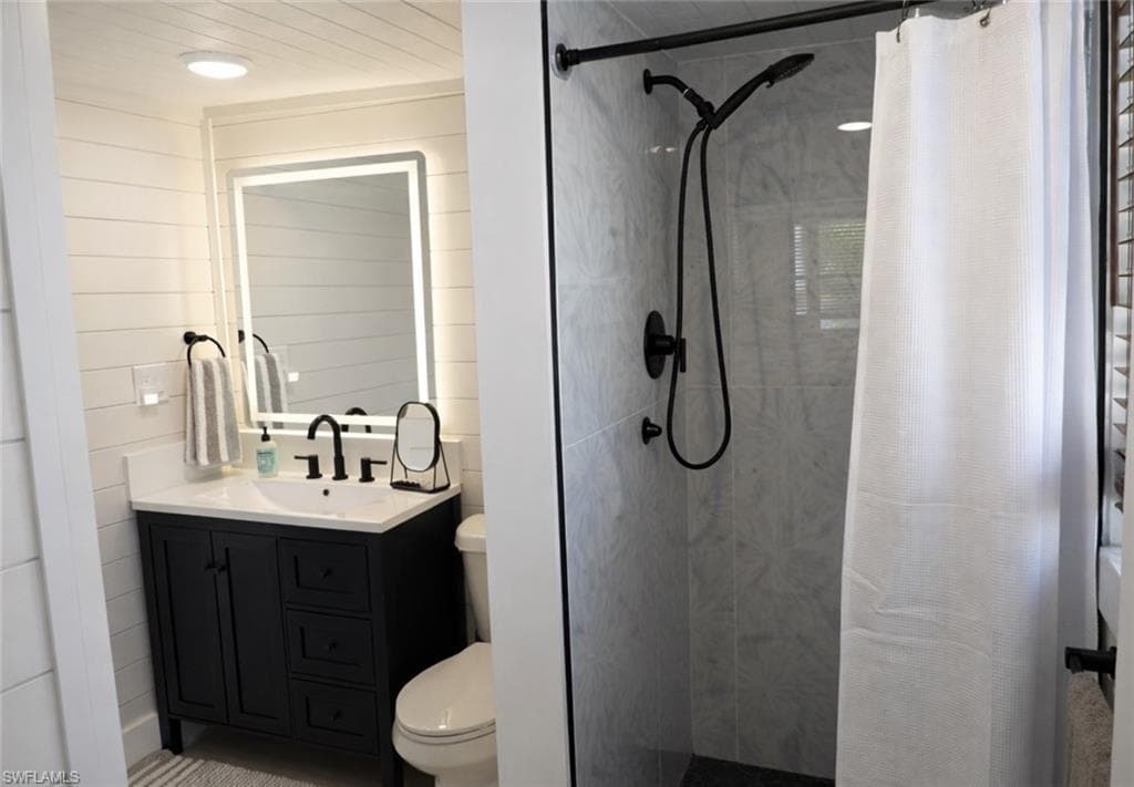 Bathroom featuring a dark wood-finish vanity with a white countertop and rectangular sink, an illuminated mirror, and a shower with light-toned tiled walls and dark-finish fixtures