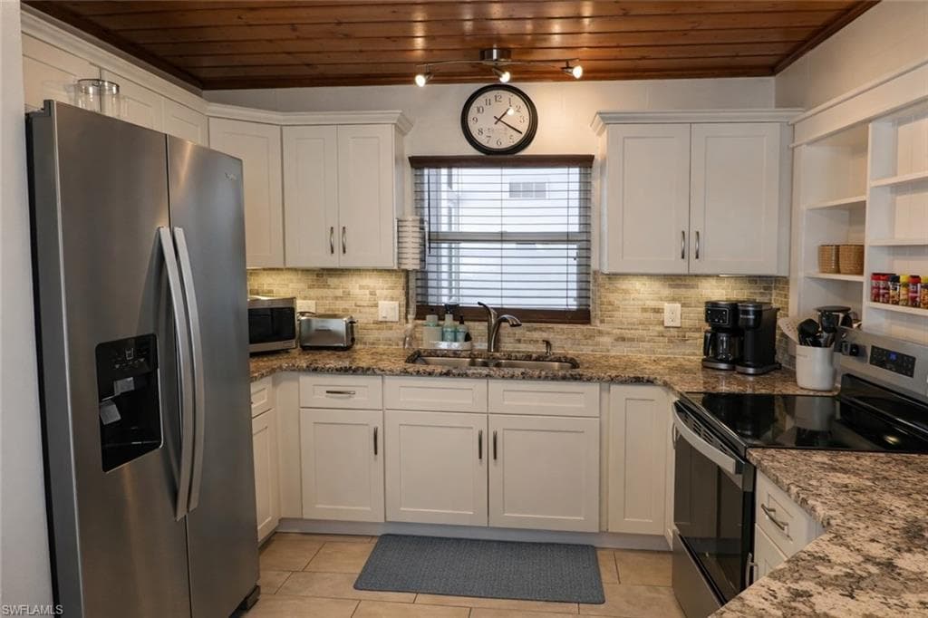 Kitchen featuring a wood-finish ceiling, stainless steel appliances, white cabinetry, a tiled backsplash, and granite countertops