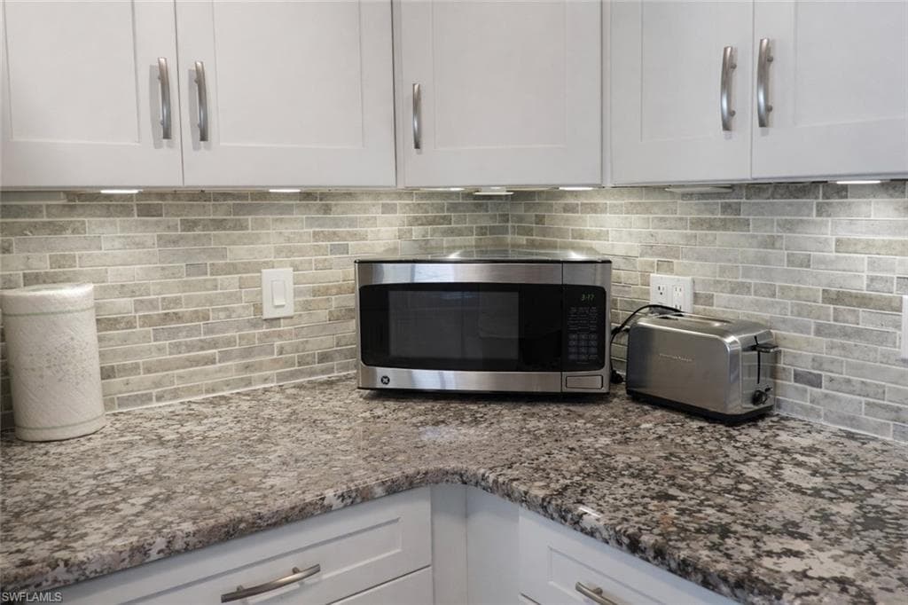 Kitchen featuring granite-style countertops, white shaker-style cabinetry with brushed nickel hardware, and a mosaic tile backsplash