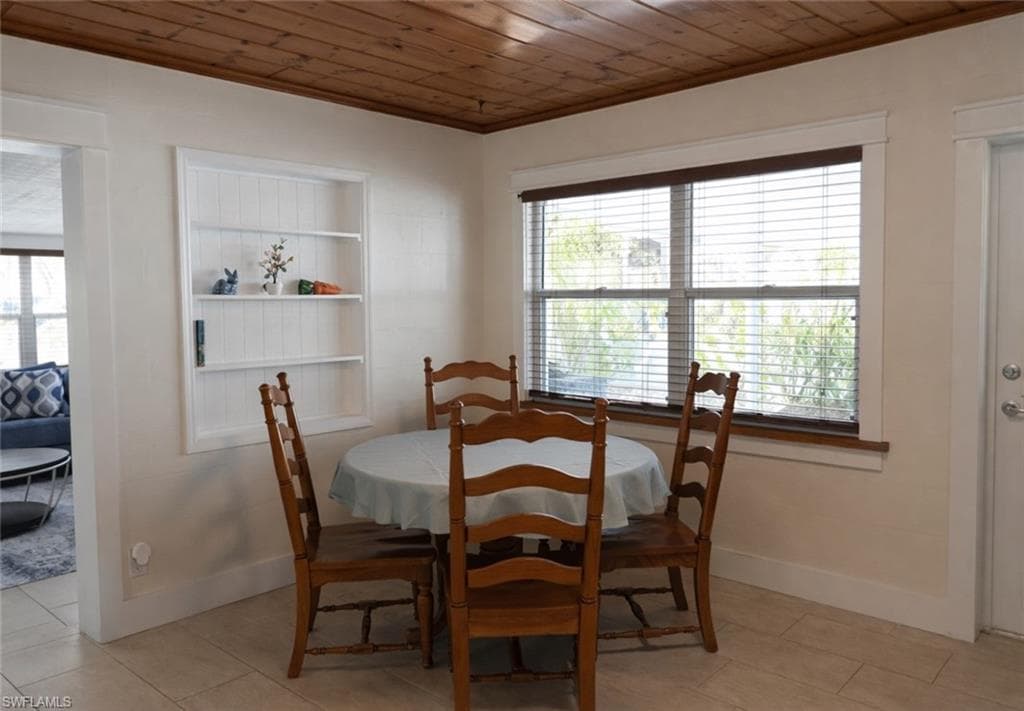 Dining area featuring a wood-panel ceiling, built-in shelving, a double window with wood-finish blinds, and tile flooring