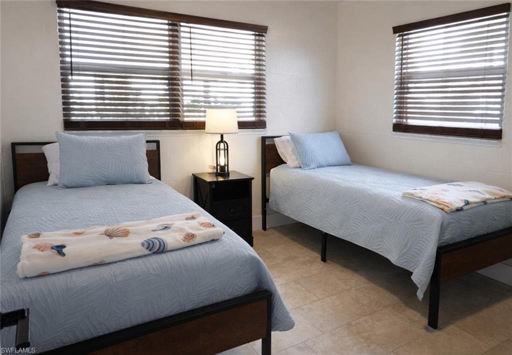 Room featuring two windows with wood-finish blinds, light-colored wall paint, and floor tiles