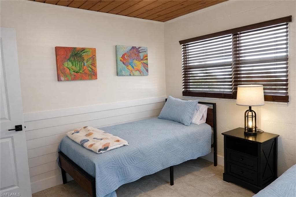 Room featuring wood-finish ceiling, light-toned walls with shiplap wainscoting, and a window with dark wood blinds